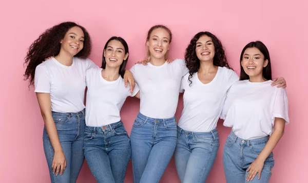Cinco mulheres jovens mistas sorridentes abraçando em pé sobre fundo rosa — Fotografia de Stock