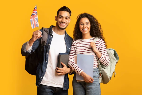 Estudar no estrangeiro. Jovem árabe homem e mulher com mochilas segurando bandeira britânica — Fotografia de Stock