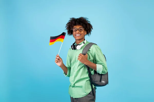 Educación moderna e intercambio de conocimientos. Africano americano adolescente chico con mochila y pequeña bandera de Alemania, fondo azul — Foto de Stock