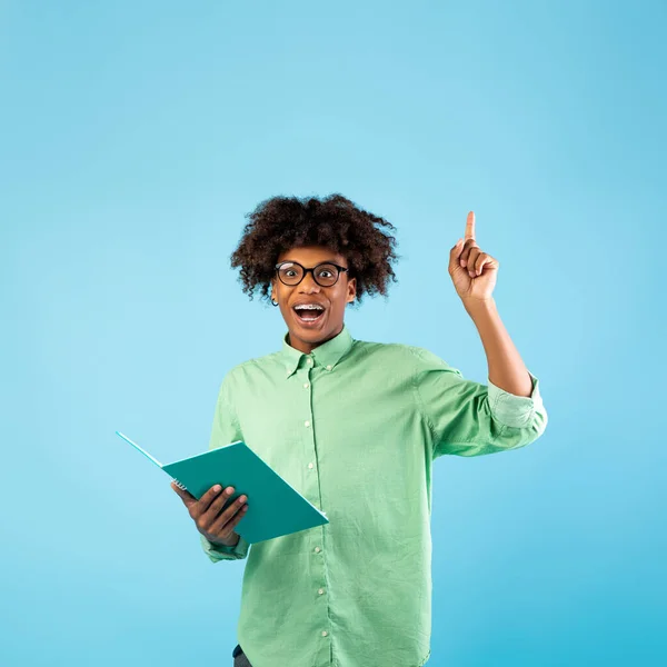 Inspiración o momento eureka. Feliz estudiante adolescente negro apuntando con el dedo hacia arriba, teniendo idea creativa, fondo azul —  Fotos de Stock