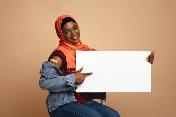 Mulher muçulmana afro-americana alegre foi vacinada, mostrando cartaz vazio — Fotografia de Stock