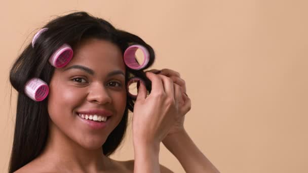 Afro-américaine femme curling cheveux appliquer des bigoudis sur fond beige — Video