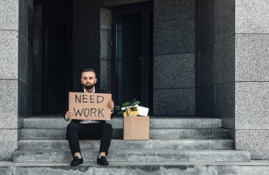 Erkek ofis çalışanı, elinde plaketle merdivenlerde özel eşyalarıyla kutunun yanında otururken işten çıkarıldı.