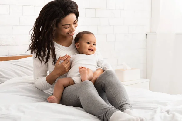 Mãe negra brincando com bebê infantil sentado na cama interior — Fotografia de Stock