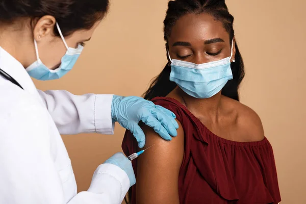 Enfermeira em vestuário de trabalho fazendo vacinação para senhora negra — Fotografia de Stock