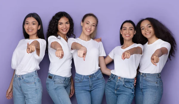 Gemengde vrouwen wijzen vingers naar camera poseren samen, paarse achtergrond — Stockfoto