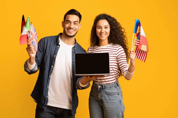 Glimlachend Arabisch paar met internationale vlaggen en laptop computer met blanco scherm — Stockfoto