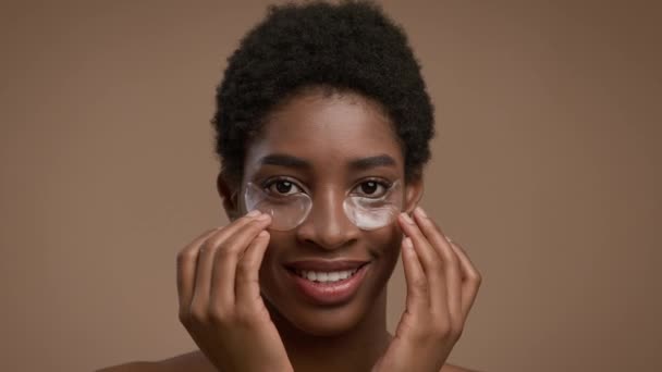Atraente preto feminino aplicando remendos sob os olhos sobre fundo bege — Vídeo de Stock