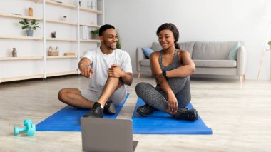 Siyah çift spor salonundan sonra dinleniyor, çevrimiçi video dersi izliyor, ekrana işaret ediyor, egzersiz programını tartışıyor.