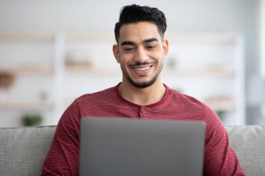 Evde dizüstü bilgisayar kullanan Ortadoğulu bir adamın yakın çekimi.