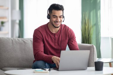 İnternetteki web sitesine katılan mutlu Arap adam, dizüstü bilgisayar ve kulaklık kullanıyor.