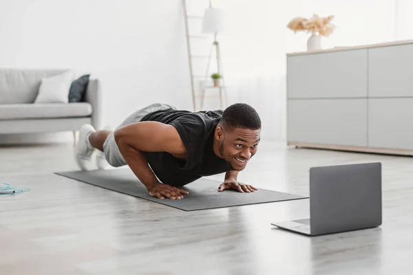 Athletic African Guy ćwiczenia na laptopie robi pompki w domu — Zdjęcie stockowe