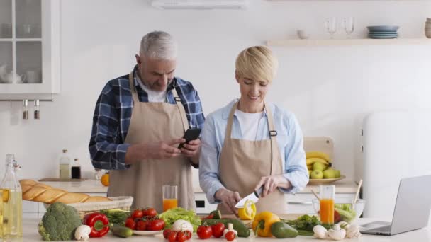 Mari tirant sur le téléphone pendant que la femme prépare le dîner dans la cuisine — Video