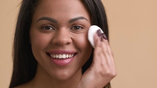 Mujer africana usando almohadilla de algodón aplicando polvo facial, fondo beige — Vídeos de Stock