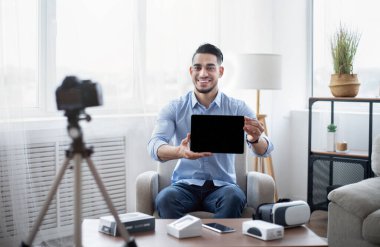 Arap erkek etkili, evdeki profesyonel dslr kamerayla modern tablet bilgisayarın video incelemesini çekiyor.