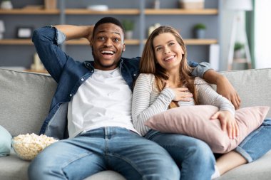 Boş zamanlarında çiftler. Mutlu Irklar Arası Aşıklar TV izliyor ve evde patlamış mısır yiyor.