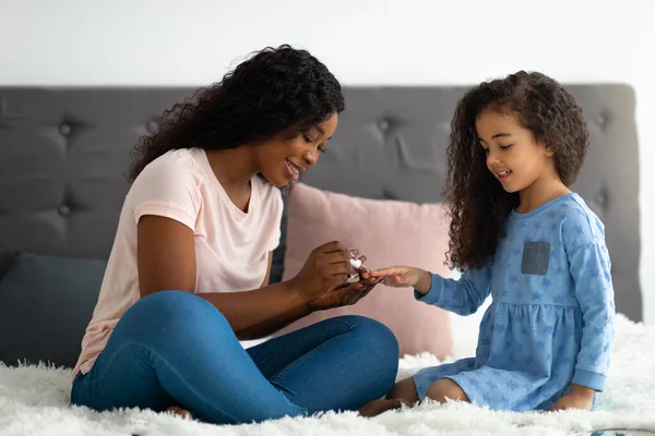 Junge schwarze Mutter trägt Lack auf ihre entzückenden Töchter Nägel auf dem Bett zu Hause, volle Länge — Stockfoto