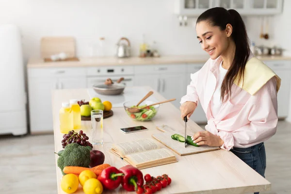 샐러드를 요리하고 주방에서 요리 책을 사용하는 여자 — 스톡 사진