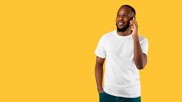Afroamerikaner spricht auf dem Handy und schaut weg, gelber Hintergrund — Stockfoto