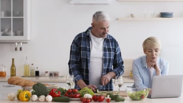 Coppia matura che cucina la cena utilizzando il computer portatile in cucina a casa — Video Stock