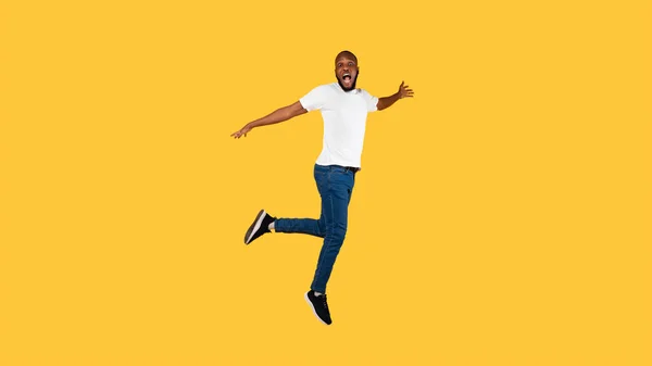 Geschokte Afro-Amerikaanse man springt kijkend naar camera, gele achtergrond — Stockfoto