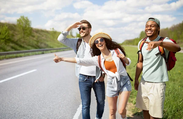 Diverse vrienden die langs de weg staan, auto 's stoppen, gratis liften, genieten van de zomervakantie Stockfoto