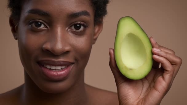 Black Woman Holding Avocado Half Near Face On Beige Background — Stok Video