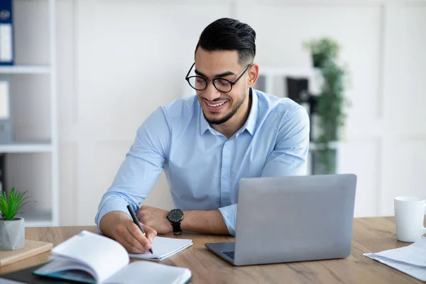 Arabischer männlicher Unternehmer schreibt Informationen während eines Online-Geschäftstreffens im modernen Büro auf — Stockfoto