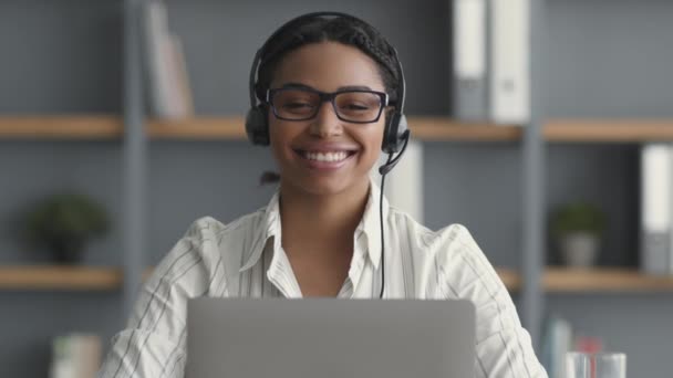 Operador de línea de ayuda. Amistosa mujer afroamericana con auriculares con micrófono sonriendo ampliamente a la cámara — Vídeos de Stock