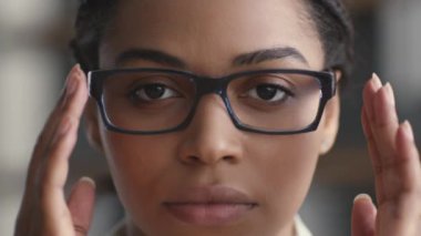 Bayan patron. Genç, kendine güvenen Afrikalı Amerikalı kadın gözlüklerini düzeltiyor, kameraya ciddi ciddi bakıyor, ağır çekimde.