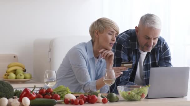 Modern mutfakta dizüstü bilgisayar ve kredi kartı kullanan orta yaşlı bir çift. — Stok video