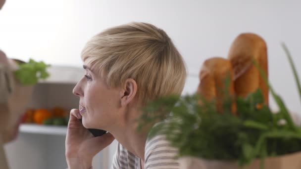 Soția vorbind la telefon, soțul despachetează după cumpărături în interior — Videoclip de stoc