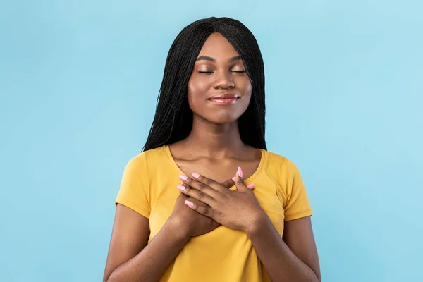 Вдячна афроамериканська жінка тисне руки на груди, на синє тло — стокове фото