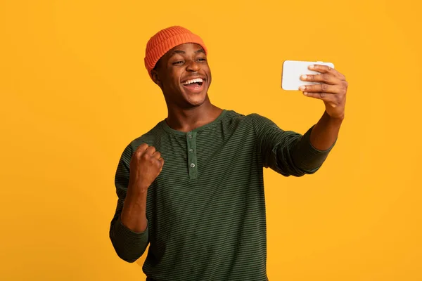 Online-Gewinn. Fröhlicher Schwarzer blickt auf Smartphone-Bildschirm und feiert Erfolg — Stockfoto