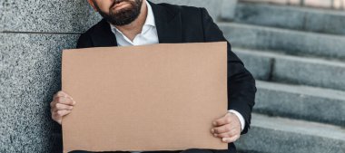 İş arama konsepti. Tanınmayan bir iş adamı elinde boş bir karton levha, dışarıda, merdivenlerde oturuyor.