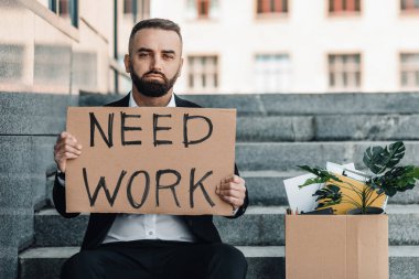 İşe ihtiyacım var. Depresyondaki olgun iş adamı posterleri ve kişisel eşyalarıyla merdivenlerde otururken kovuldu.