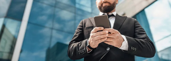 Aplicação empresarial. Empreendedor confiante homem usando smartphone, de pé contra edifício de escritórios, colheita, panorama — Fotografia de Stock