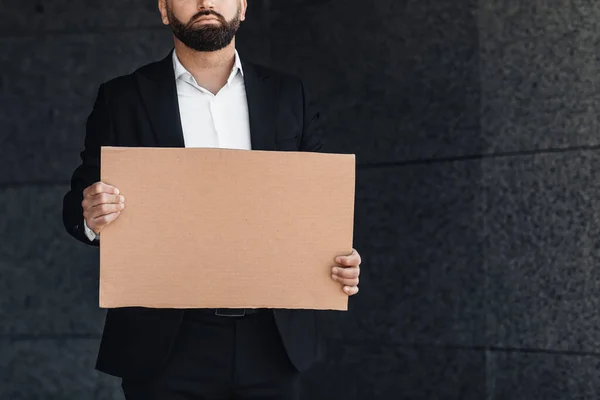 Trabalhador de escritório masculino irreconhecível em terno segurando sinal de papelão em branco em pé ao ar livre, espaço livre, cultura — Fotografia de Stock