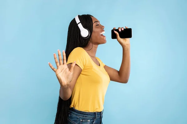 Afrikai amerikai hölgy éneklés holding telefon közel Mouth, kék háttér — Stock Fotó
