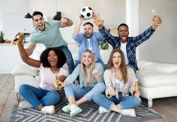 Emocionados diversos amigos viendo fútbol, sosteniendo la pelota de fútbol, gritando META, animando a su equipo favorito en casa — Foto de Stock