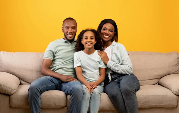 Gelukkige familie. Portret van liefhebbende Afrikaanse Amerikaanse moeder, vader en dochter zittend op een bank over gele achtergrond — Stockfoto