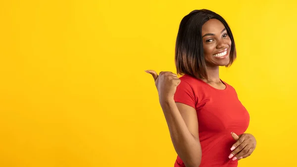 Černá žena ukazující palec pryč na volném místě, žluté pozadí — Stock fotografie