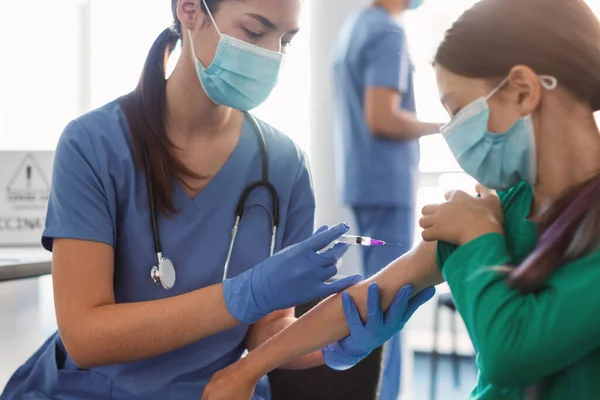 Niña de la escuela que recibe la inyección de la vacuna contra el Coronavirus sentada con el médico en interiores — Foto de Stock