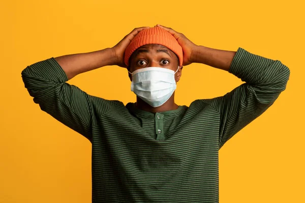 Coronavirus Panik. Rädd afroamerikansk man i medicinsk mask berörande huvud med chock — Stockfoto