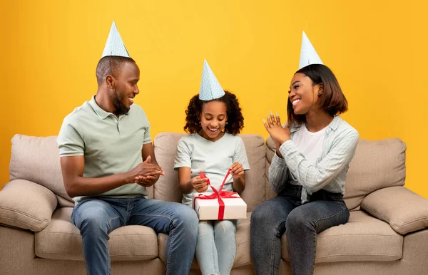 Spännande afrikanska amerikanska föräldrar gör överraskning för sin vackra dotter, ger present låda, hälsning med födelsedag — Stockfoto