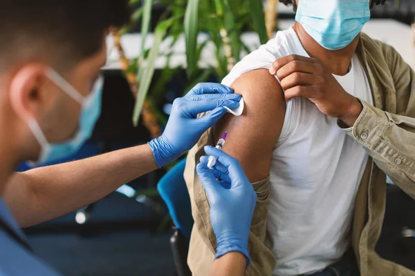 Black Man ontvangt Covid Vaccine Injectie Zittend met Doctor Indoor — Stockfoto