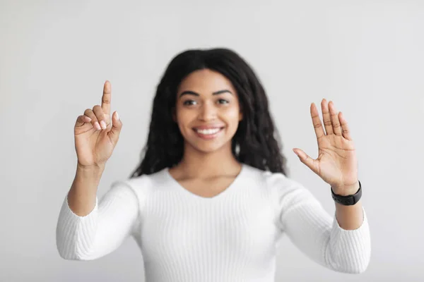 Mujer negra feliz usando la pantalla virtual para el trabajo, pulsando el botón en la pantalla invisible sobre la pared de luz —  Fotos de Stock