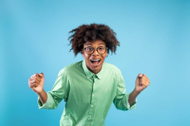 Evet, başardım. Aşırı neşeli Afro-Amerikalı adam, sıkılmış yumruklarını sallıyor, neşeli ve neşeli başarı, mavi arka plan