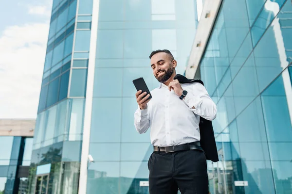 Estilo de vida empresarial. Empreendedor maduro com smartphone na mão conversando com o cliente, de pé contra o centro de escritório — Fotografia de Stock