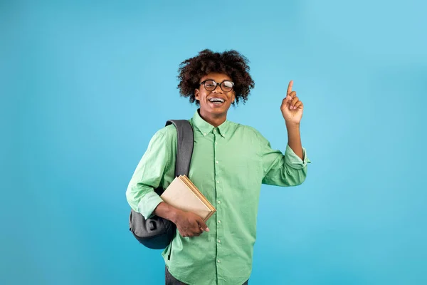 Ena, Eureka. Extasiado afro-americano estudante cara tendo ideia criativa, apontando o dedo para cima no fundo do estúdio azul — Fotografia de Stock